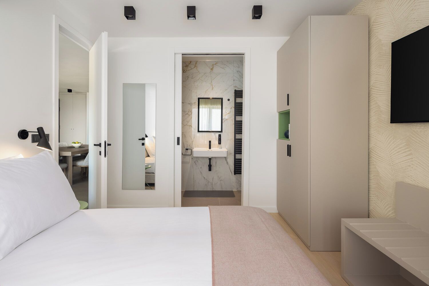 Een moderne slaapkamer met een bed, een inloopkast, een badkamer met een marmeren wastafel en een tv aan de muur.