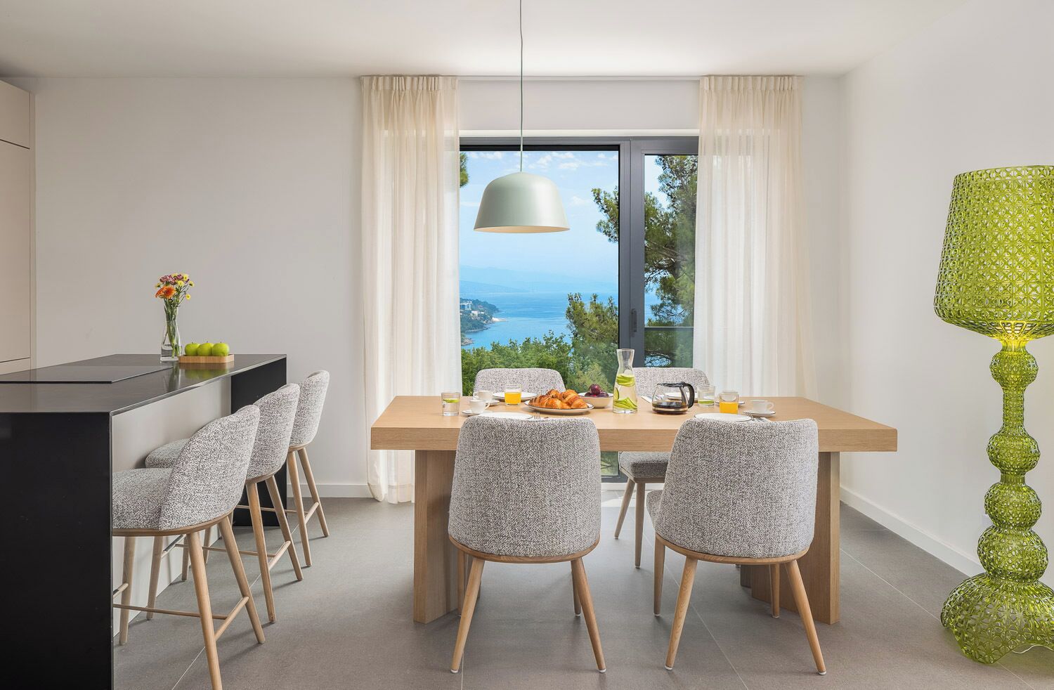 Un comedor con vistas al mar, una mesa dispuesta para el desayuno y una lámpara decorativa verde.