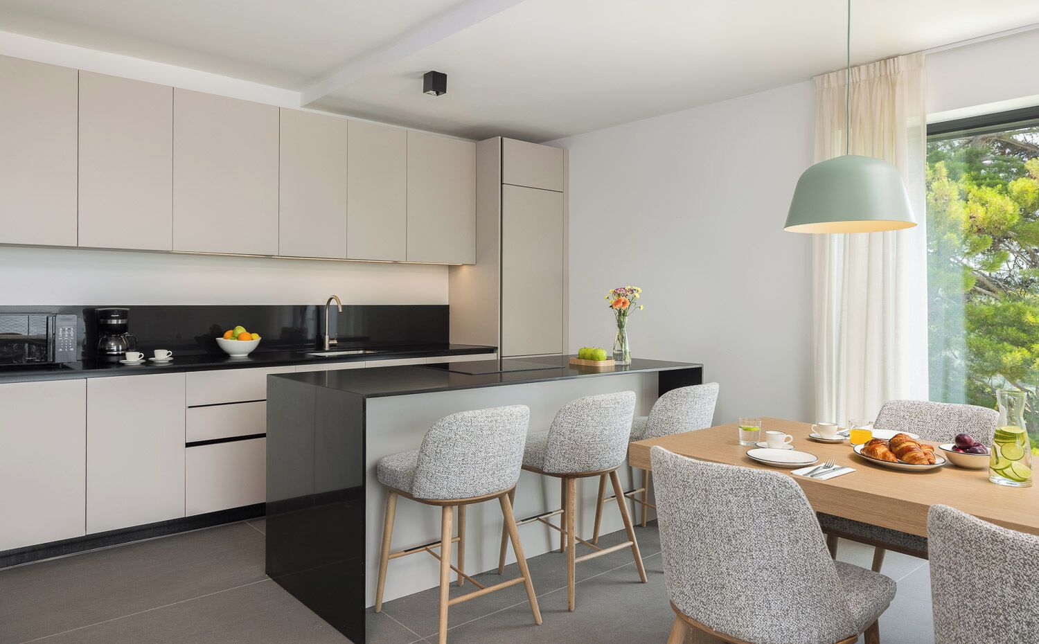 A modern kitchen with a central island, bar stools, and a dining table set for breakfast.