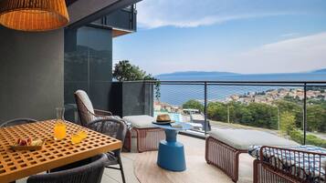 Un balcone con mobili in vimini, un tavolo con bevande e vista su una cittadina costiera.