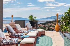 A terrace with wicker furniture, a view of a lake, and a town in the background. - Aminess Younique Vollo Hotel Residences (Opatija)