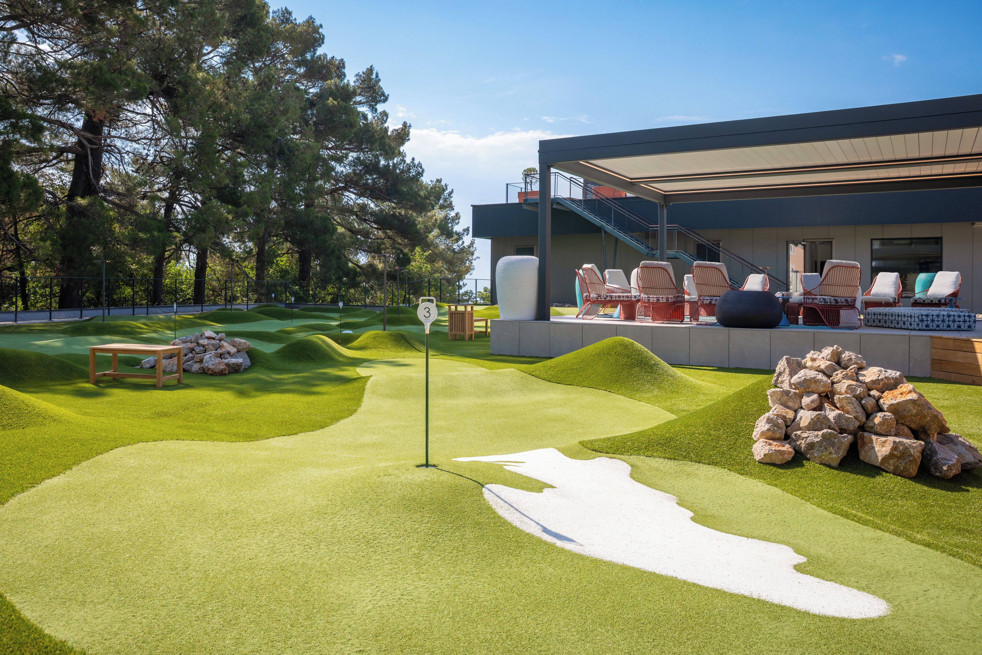 A modern building with a rooftop deck featuring outdoor seating and a putting green.
