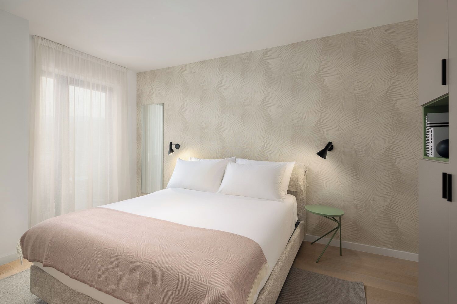 Ein Schlafzimmer mit einem Bett, einem Nachttisch, einer Lampe und einer Wand mit einem Blattmuster.