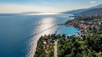 An aerial view of a coastal town with a marina, dense greenery, and a clear view of the sea.