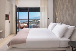 Un dormitorio con una cama grande, vistas a la ciudad a través de una puerta corredera y un balcón con mobiliario exterior.