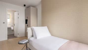 Ein modernes Hotelzimmer mit einem Bett, einem Nachttisch, einem Kleiderschrank und einem durch eine offene Tür einsehbaren Badezimmer.