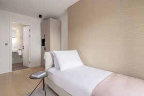 Una habitación de hotel moderna con cama, mesita de noche, armario y baño visible a través de una puerta abierta.