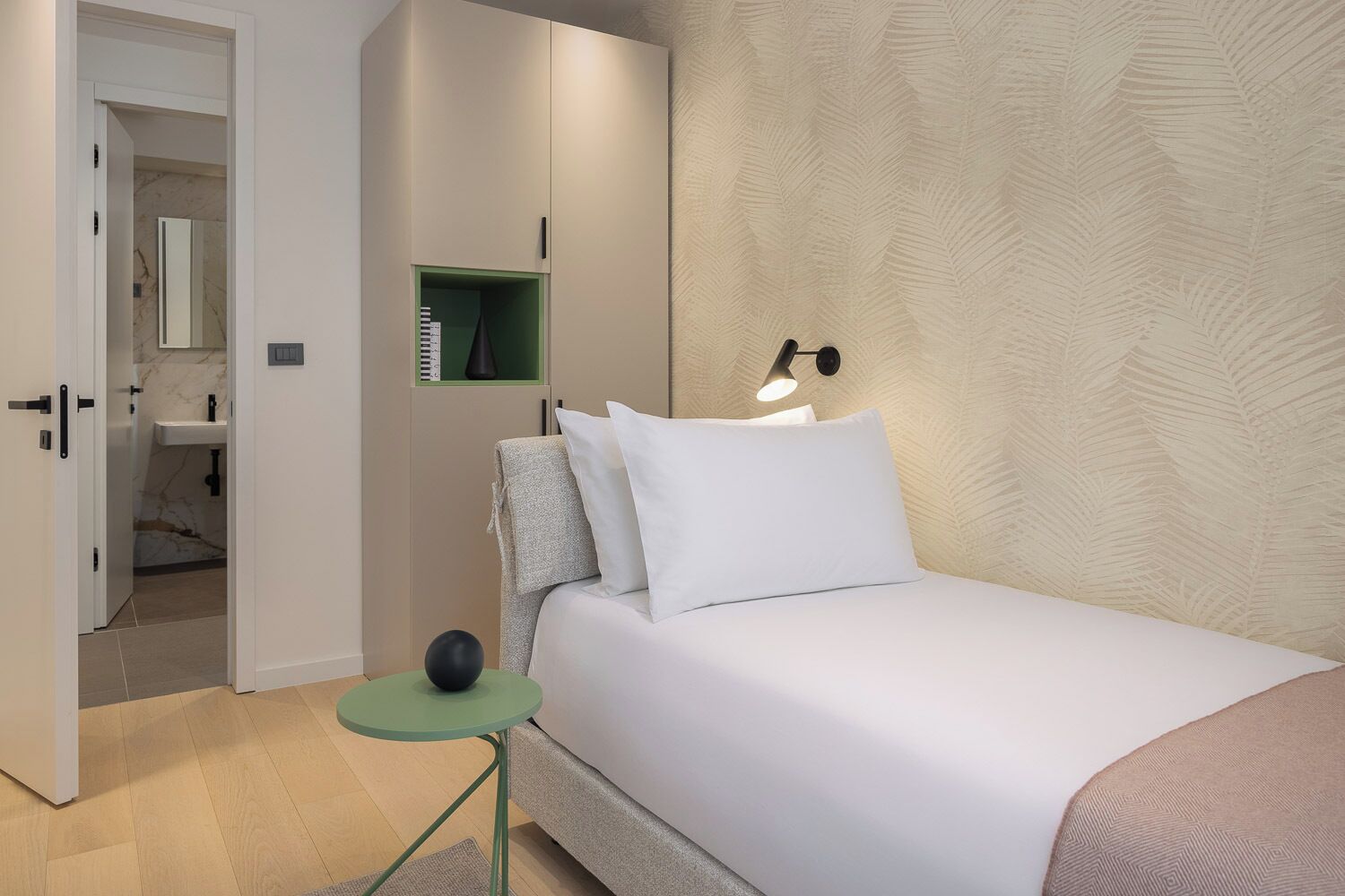 A bedroom with a bed, bedside table, lamp, wardrobe, and a mirror.