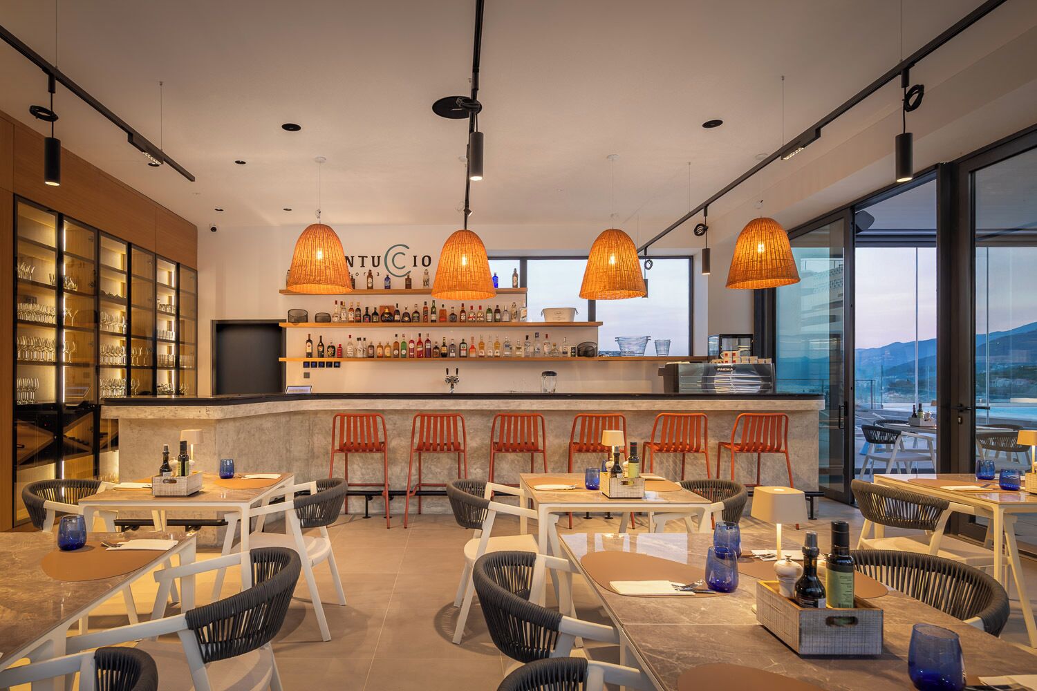 A modern bar area with a bar counter, seating, and a view of the outdoors.