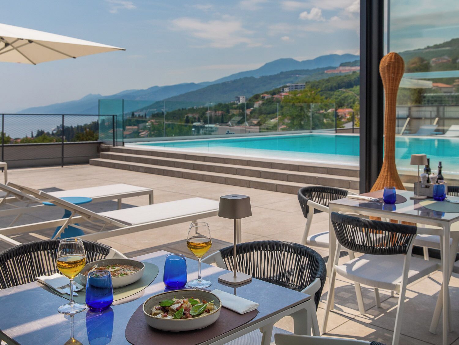 Un espace de restauration sur le toit, avec vue sur la piscine, des sièges en plein air et une table dressée pour deux personnes.
