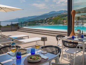 Comedor en la azotea con vista a la piscina, asientos al aire libre y una mesa lista para dos personas.