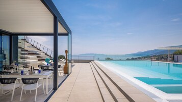 Zona de piscina en la azotea con barandilla de cristal, mobiliario exterior y vista al mar.