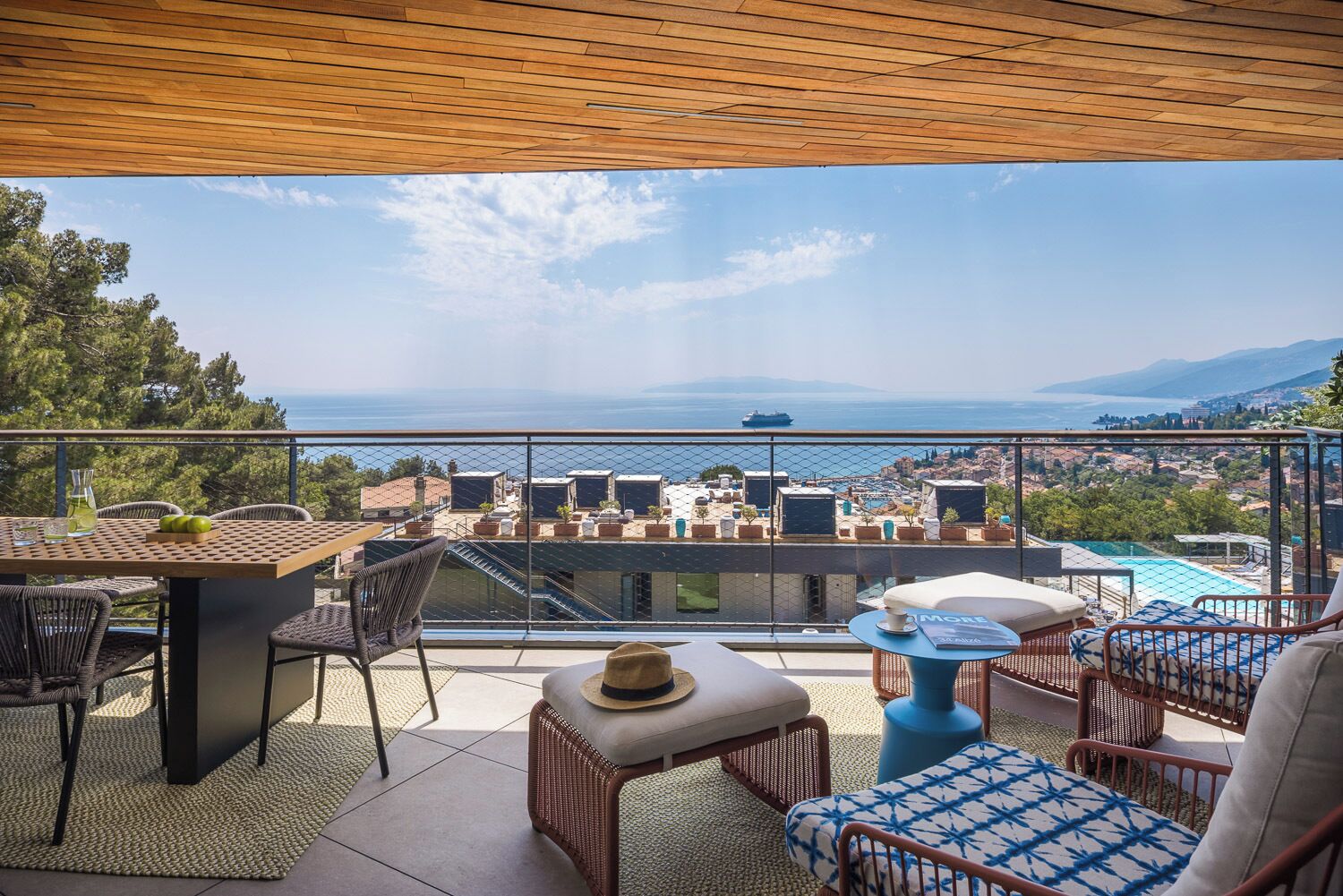 Un balcón con una mesa, sillas y vistas al mar y al paisaje urbano.