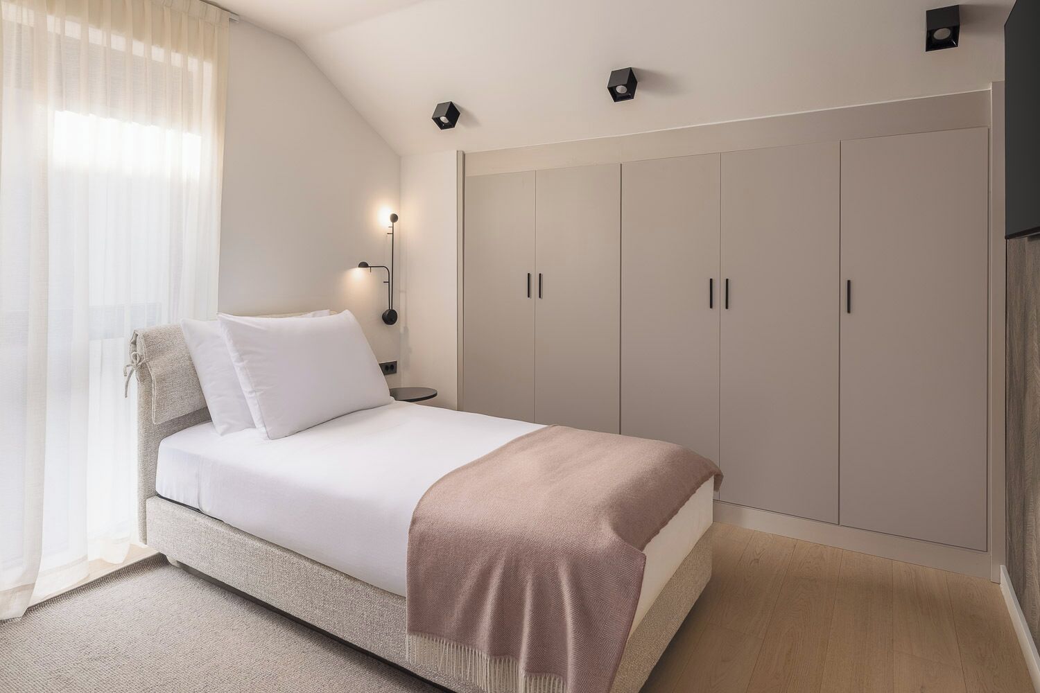A bedroom with a bed, a wardrobe, a bedside table, and a lamp.