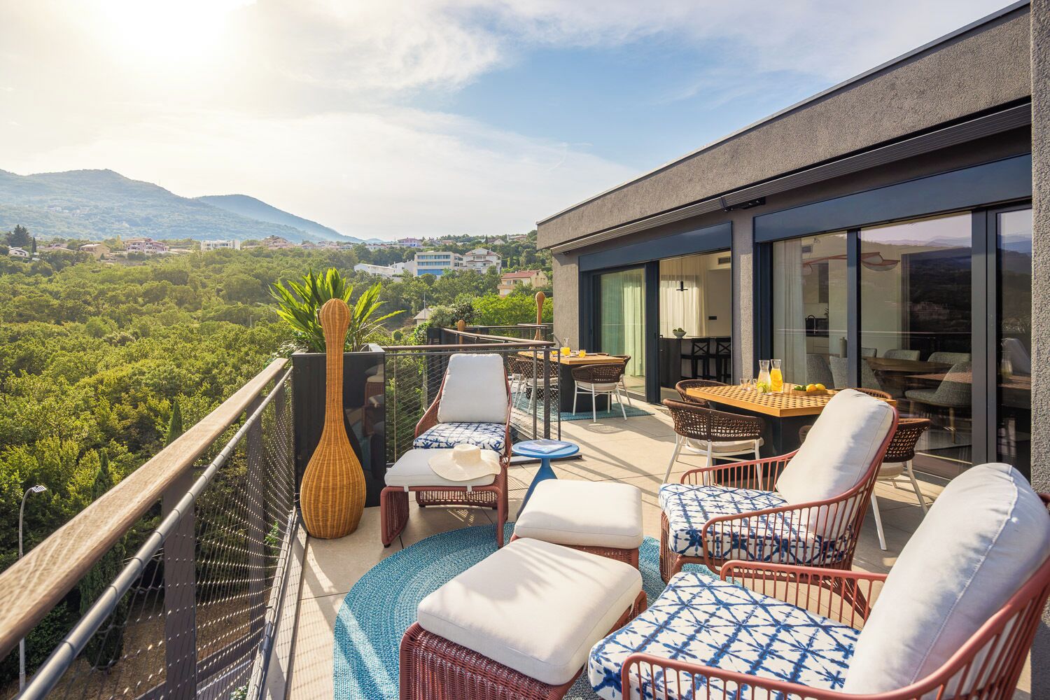 Un balcón con mobiliario de mimbre, una mesa de vidrio y vistas a un paisaje montañoso.