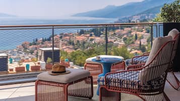 Un balcón con mobiliario de mimbre, una mesa y vistas a una ciudad costera.