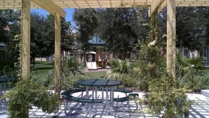 A covered outdoor area with a table and chairs, surrounded by greenery and a playground in the background. - Luxury Resort Townhome- 3 miles to Disney- Low Price- Online Booking (Kissimmee)