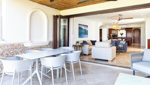 Ein modernes Wohnzimmer mit Esstisch, weißen Stühlen, einer Couch und einer Küche im Hintergrund.