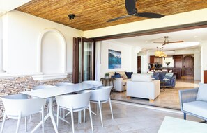 Un espace de vie moderne comprenant une table à manger, des chaises blanches, un canapé et une cuisine en arrière-plan.