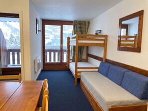 A room with a bunk bed, a sofa, a table, and a window with a view of snow-covered mountains. - (AL-203) Val Thorens - Ski In/Out - 5 Beds Flat (Les Belleville)