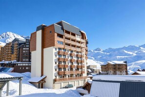 A multi-story hotel with balconies, set against a backdrop of snow-covered mountains. - (AL-203) Val Thorens - Ski In/Out - 5 Beds Flat (Les Belleville)