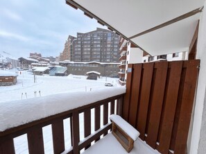 Lumipeitteinen parveke, jossa on puinen kaide ja taustalla näkyy korkea kerrostalo.