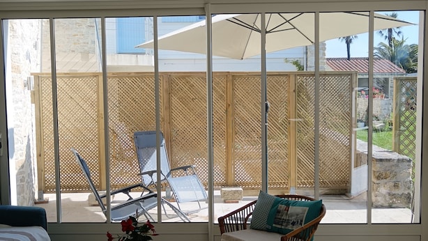 Eine sonnendurchflutete Terrasse mit Korbmöbeln, einem Holztisch und Blick auf eine Steinmauer und einen Außenbereich mit Sitzgelegenheiten.