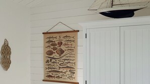 Ein Zimmer mit weißer Wand, einem Holztisch mit Schubladen, einer Wandillustration mit einem Fisch und einem Modell eines Segelbootes.