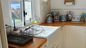 Eine Küche mit einer Steinwand, einem Fenster, einer Spüle, einem Wasserkocher, einem Toaster und einem Holzboden mit Küchenutensilien.