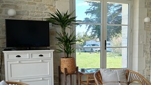 Ein gemütliches Wohnzimmer mit Steinwand, Fernseher, Korbmöbeln und Blick ins Freie.