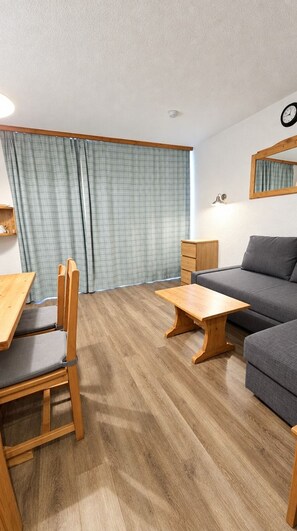 Ein Zimmer mit Holzboden, einem grauen Sofa, einem Holztisch, einem Stuhl und einer kleinen Holzkabine.