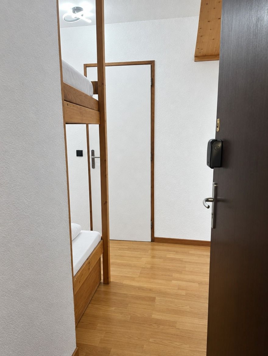 A room with a bunk bed, a door with a lock, and a wooden floor.