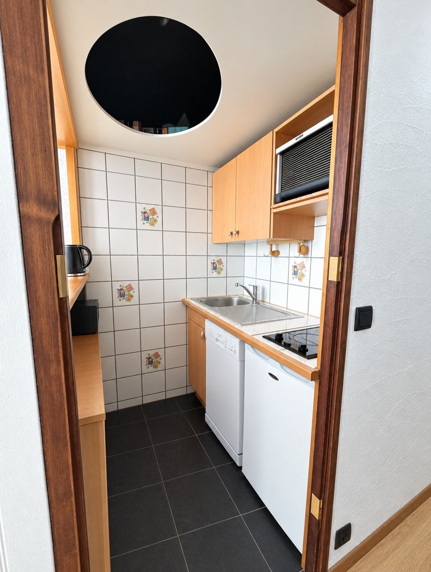 Eine kleine Küche mit Spüle, Herd und Geschirrspüler, mit Fliesenrückwand und Holzschränken.