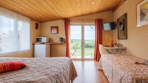 Una habitación con dos camas, una kitchenette pequeña, un televisor y una puerta corrediza de vidrio al exterior.