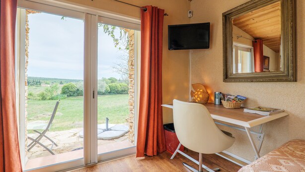 Habitación con escritorio, silla, televisor y puerta corrediza de vidrio que da a un espacio exterior.