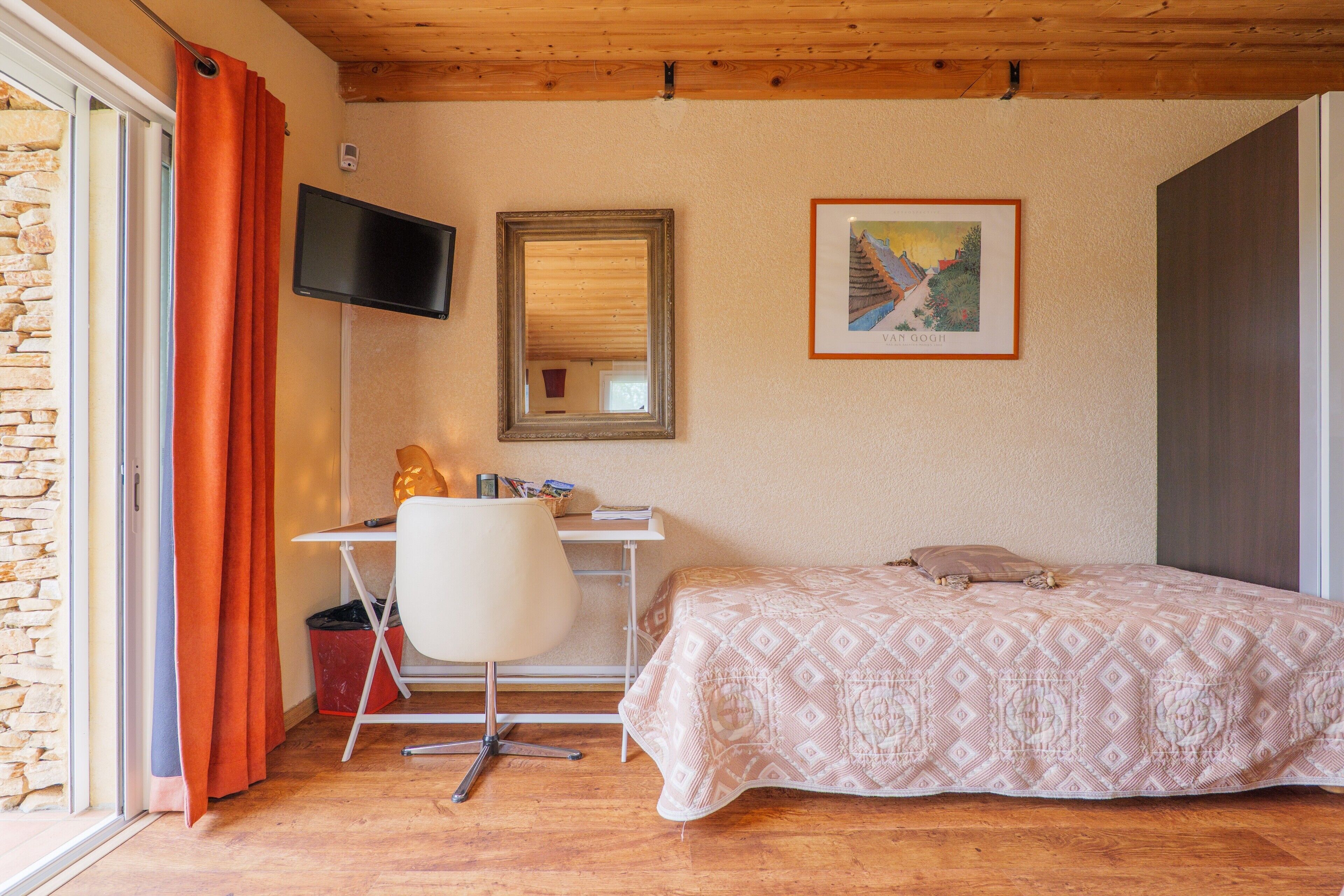Een slaapkamer met een bed, een bureau, een stoel, een televisie en een schilderij aan de muur.