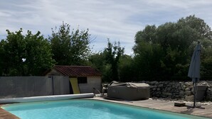 Una piscina con cubierta de madera, un área de estar techada y un muro de piedra al fondo.