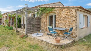 Una casa de piedra con un patio, una pérgola y una mesa con sillas.
