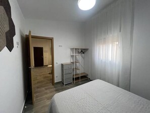 Ein Schlafzimmer mit Bett, Kleiderschrank, Schreibtisch und einer Tür zu einem anderen Raum.