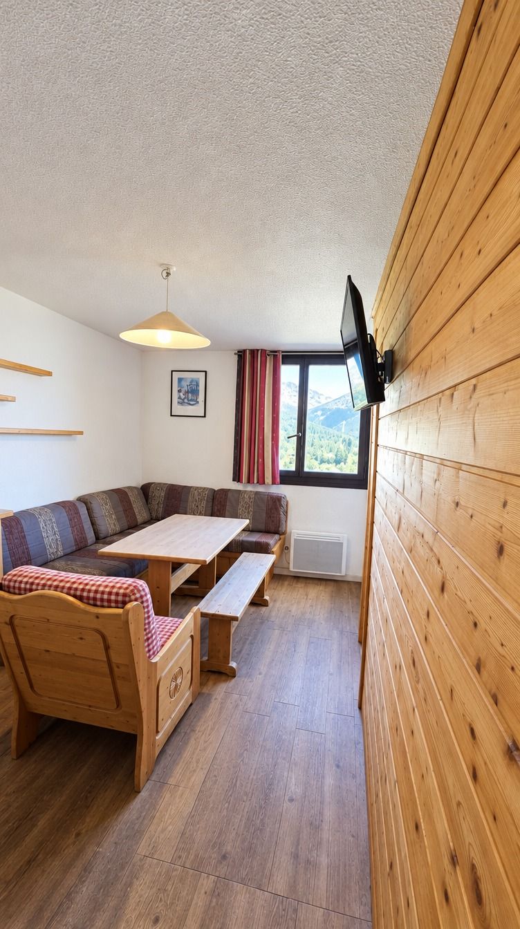 Une pièce chaleureuse avec un banc en bois, une table et un téléviseur fixé au mur.