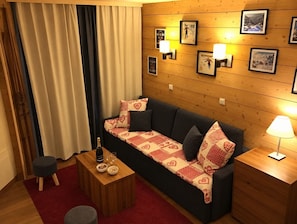 A cozy room with a sofa, a wooden nightstand, a small table with a bottle and glasses, and a red rug. - Val Thorens - Ski In/Out - 5 Beds Flat (M-603) (Les Belleville)