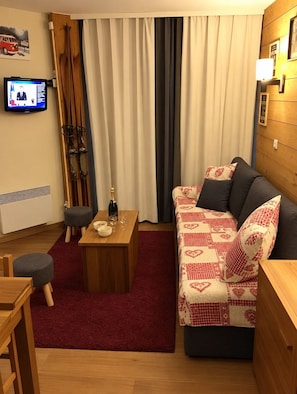 Ein gemütliches Wohnzimmer mit einer Holzdirektiva, einem kleinen Tisch mit einer Flasche und Gläsern sowie einem an der Wand befestigten Fernseher.