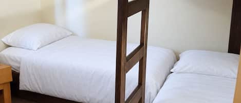 Une chambre avec un lit superposé, une tête de lit en bois, une petite table en bois et un mur sobre.
