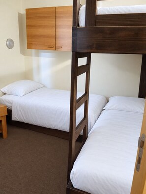 Ein Schlafraum mit Etagenbett, einem Holzkopfteil, einem kleinen Holztisch und einer schlichten Wand.