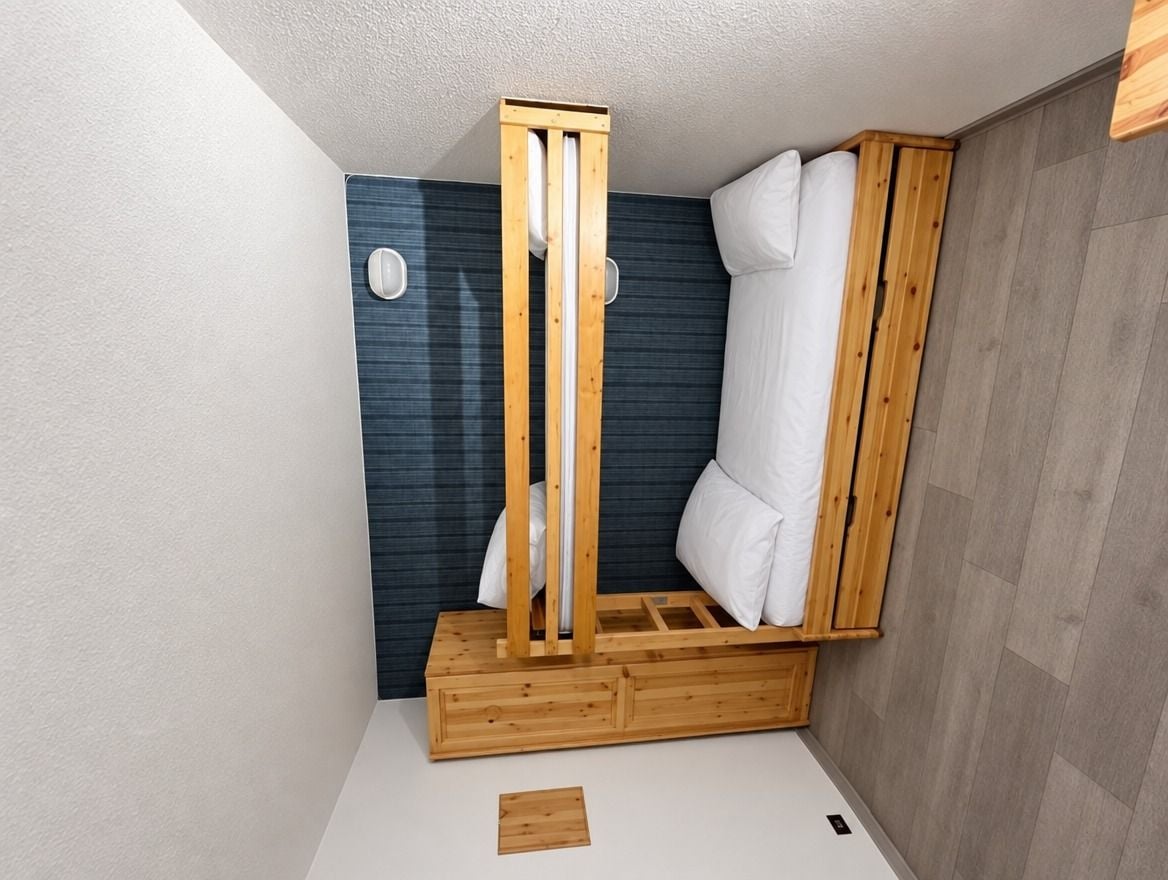 Ein kleiner, kompakter Raum mit einem Bett, einer hölzernen Bank und einer Wandleuchte.