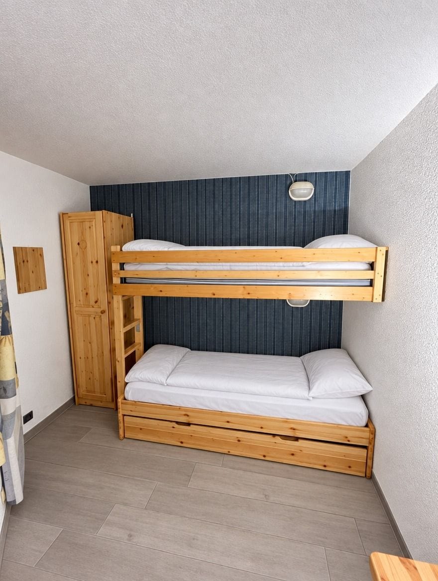 Ein Stockbett mit Holzrahmen und weißer Bettwäsche, ein Holzschrank und ein kleiner Tisch.