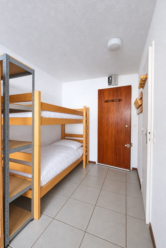 A bunk bed with a metal frame and a wooden headboard, a wooden door, and a tiled floor.