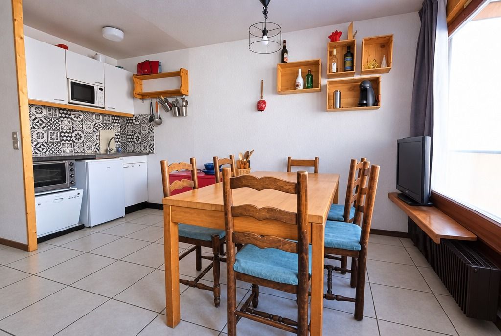Eine kleine Küche mit weißen Schränken, einer Mikrowelle, einem Backofen und einem Essbereich mit Holztisch und -stühlen.