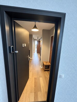 A hallway with a wooden floor, a small wooden stool, and a door with a black frame and a digital lock. - Val Thorens - Ski In/Out - 7 Beds Flat (S-K10) (Val Thorens)