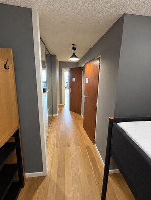 A narrow hallway with a bed on the right, a wooden wardrobe on the left, and a door at the end. - Val Thorens - Ski In/Out - 7 Beds Flat (S-K10) (Val Thorens)